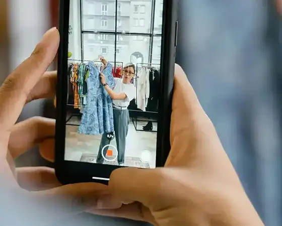 Person filmt Modepräsentation im Geschäft mit Smartphone.