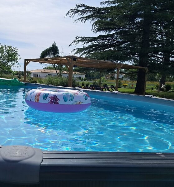 Piscine des P'tites Cagouilles – Détente et rafraîchissement garantis Piscine extérieure avec bouée gonflable colorée, entourée d’arbres et d’un abri en bois, idéale pour se rafraîchir en été au gîte Les P'tites Cagouilles.