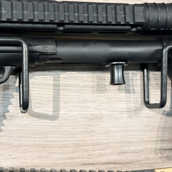 Close-up of a black AR-style rifle with a Picatinny handguard, pistol grip, and a magazine loaded with rounds visible at the right.