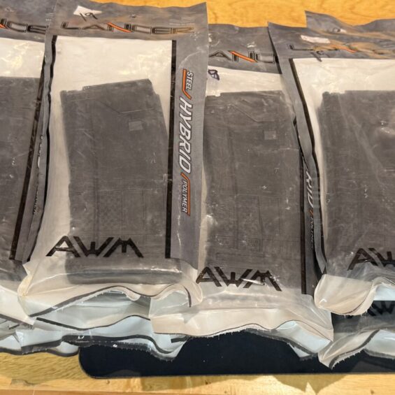 Row of gray plastic bags labeled AWM HYBRID on a wooden table, stacked side by side.