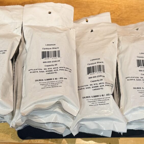 Row of white padded envelopes with barcode labels reading L5AWM20 Opaque Black on a wooden table.