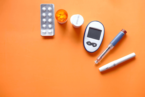medical tools and medicines for diabetes set on an orange surface