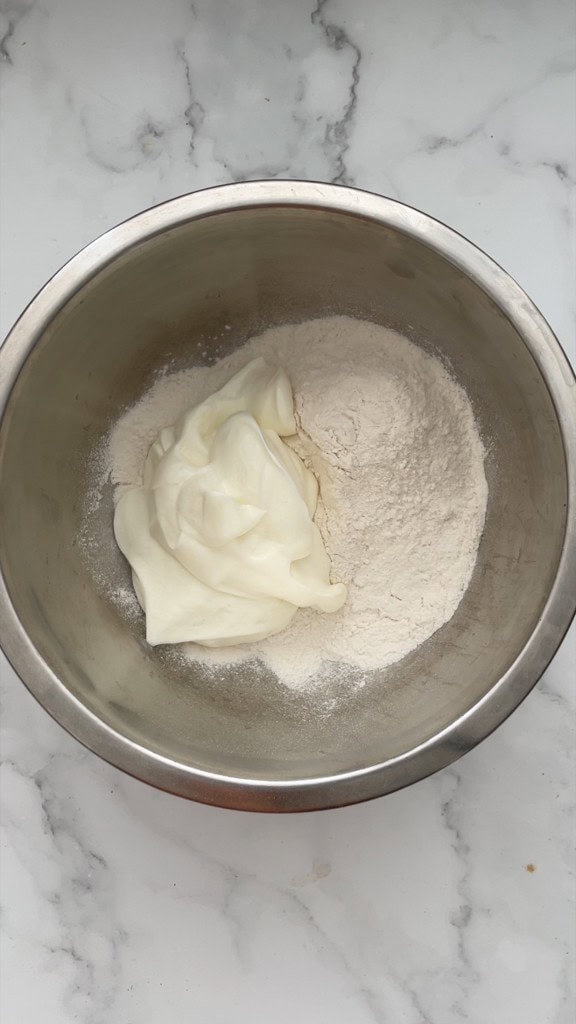 Adding flour and greek yogurt to a mixing bowl to make the pizza crust. 