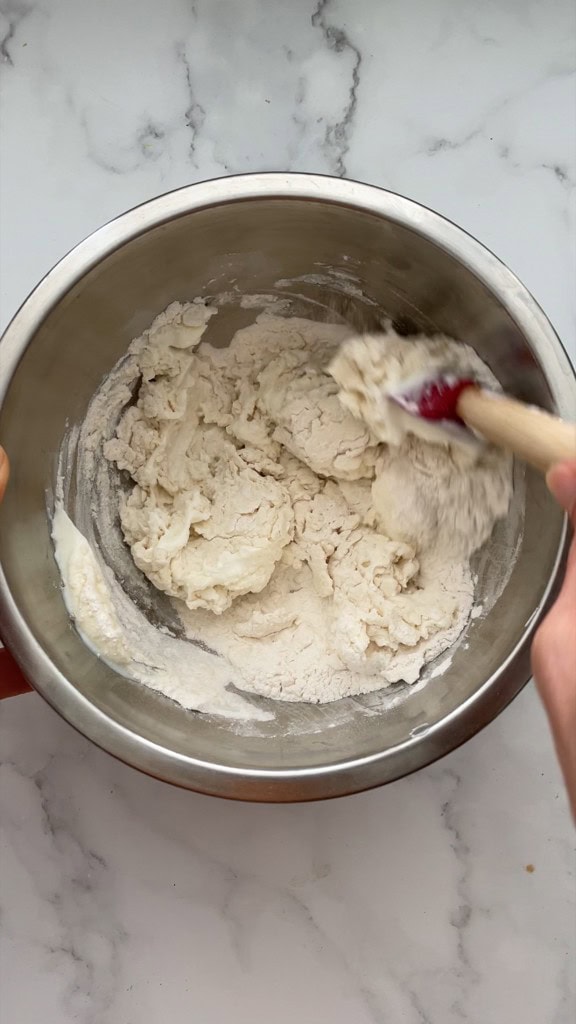 Stirring the pizza dough ingredients using a spatula. 