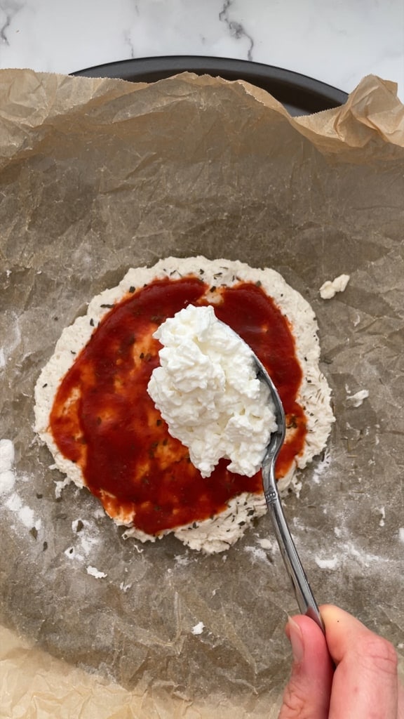 Adding cottage cheese on top of the pizza sauce. 