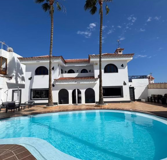 Villa mit einem Pool und Palmen in Gran Canaria unter blauem Himmel.