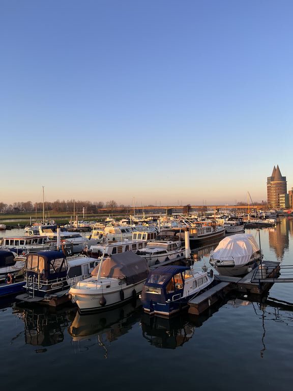 Overzicht van de haven in Roermond bij zonsondergang, met een warme gloed over het water en de omliggende gebouwen