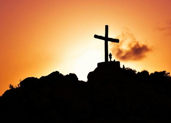 human standing beside crucifix statue on mountain