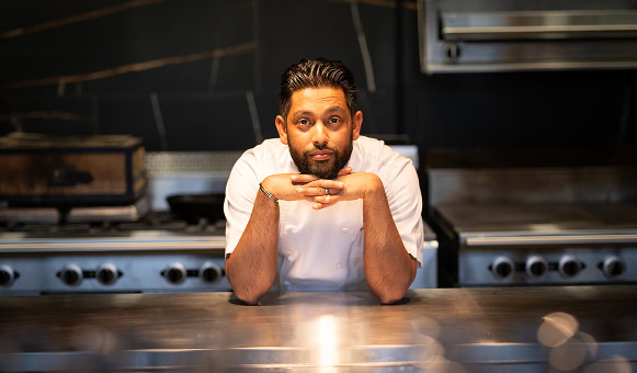 A chef in whites poses in the clean, empty kitchen of an upscale Raleigh restaurant.