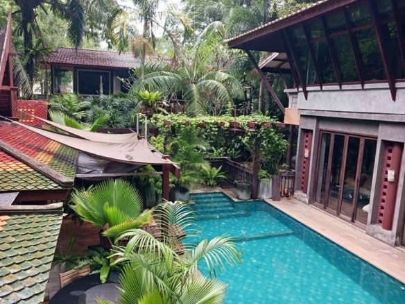 Tropical resort courtyard with turquoise swimming pool surrounded by lush palm vegetation and wooden structures
