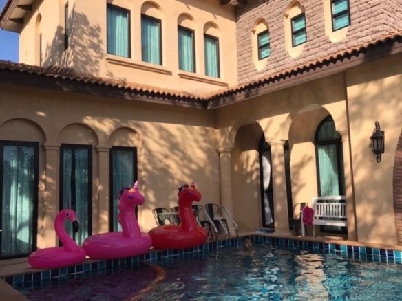 Luxurious courtyard pool with pink flamingo floats and arched colonnade