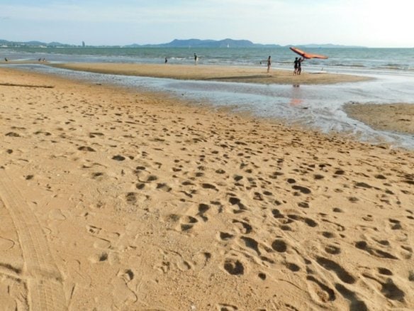 Busy beach scene with footprints in sand, surfers, and mountains