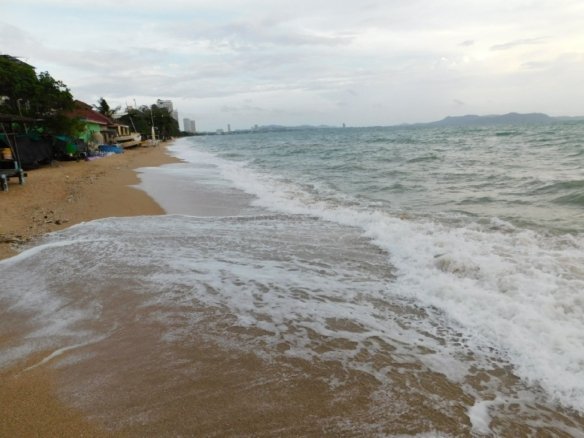 Waves washing onto sandy beach with coastal buildings and mountains in distance