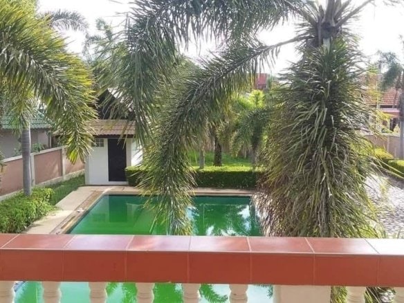 Tropical backyard with green pool surrounded by palm trees and residential houses