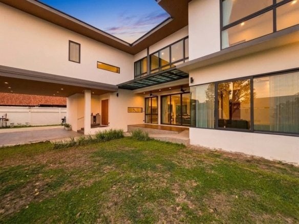 Modern two-story house with courtyard, large windows, and green lawn at dusk