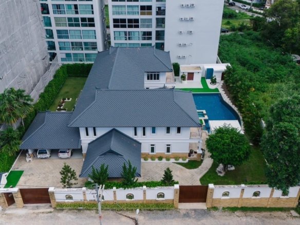 Aerial view of modern white house with dark roof and swimming pool surrounded by tall buildings