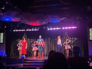 Bright stage performance featuring characters in superhero and retro costumes at 407 and Beyond Vacation Co. event.