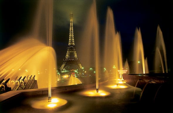 Fountains shimmering in the lights at night with the eiffel tower in the background