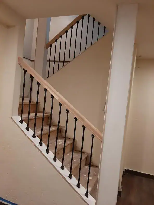 A staircase renovation in Coeur D'Alene featuring new wooden handrails and black metal balusters installed by a professional handyman.