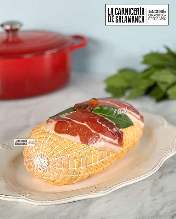 Pularda rellena sobre fuente blanca decorada con jamón, laurel, dátiles, pasas y orejones. Disponible esta carne para comprar online en La Carnicería de Salamanca.