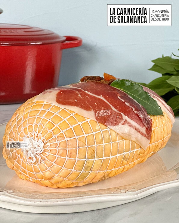 Detalle de pularda rellena sobre fuente blanca decorada con jamón, laurel, dátiles, pasas y orejones. Disponible esta carne para comprar online en La Carnicería de Salamanca.