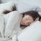 A woman dressed in white sleeping in a bed with white bedding showcasing the best comforter for hot sleepers.