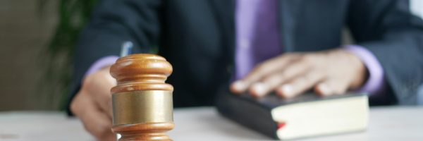Male in suit with hand on a book and holding a gavel
