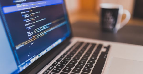 Software developer coding on a laptop with financial data on screen.