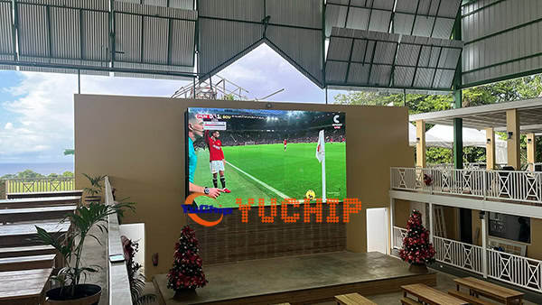Installed outdoor LED display showing a soccer match in a hotel venue decorated with Christmas trees, creating a festive holiday atmosphere in Barbados