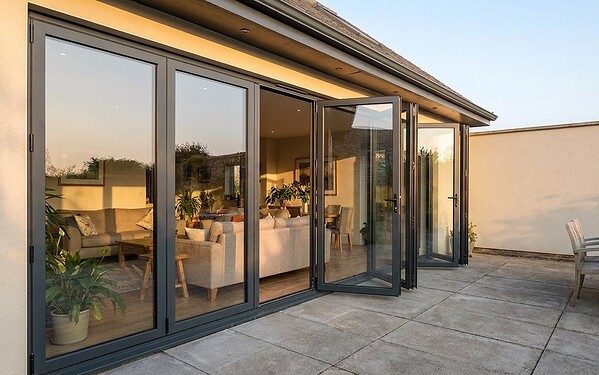 Aluminium bi-fold doors with one traffic-door leaf open for daily access onto a villa terrace at dusk