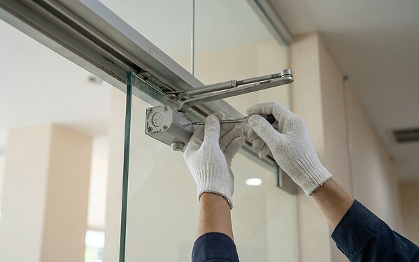 Technician adjusting an overhead door closer on a frameless glass door