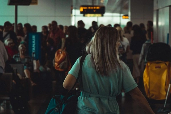Woman with backpack confidently navigating busy airport terminal with crowds of travelers and departure boards visible, representing graduated exposure to travel situations