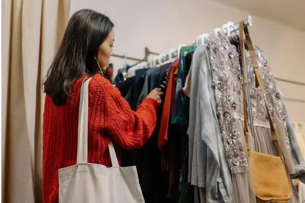 미국 50대 여성 옷 브랜드 TOP 12 (1편) 2 This image shows a woman in a red sweater selecting a clothes on a rack