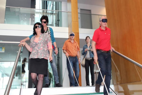 Bild: Teilnehmer einer Mitarbeiterschulung gehen über Treppe mit Sehbehinderungssimmulationsbrillen und Blindenstöcken