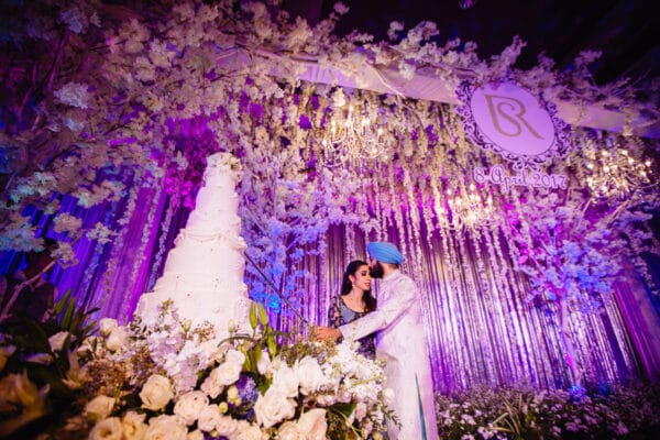 Bride and groom beside a floral wedding cake at their reception