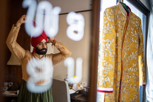 Sikh groom tying his red turban while getting ready for his wedding