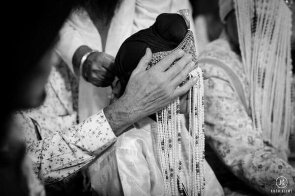 Black-and-white close-up of the groom’s sehra being tied before the Anand Karaj