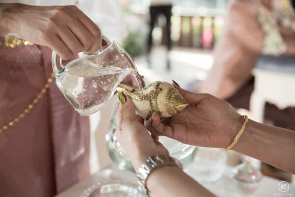 A guest pours blessed water from a conch shell over the couple's hands during Rod Nam Sang at Dusit Thani Hua Hin