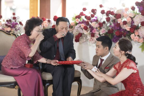 The bride in a red dress and the groom kneel to serve tea to their elders at the Chinese tea ceremony at Dusit Thani Hua Hin