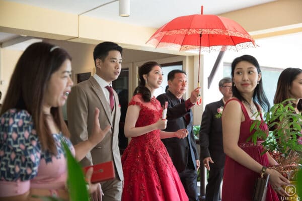 The bride in red leaves with her family under a red umbrella after the tea ceremony at Dusit Thani Hua Hin