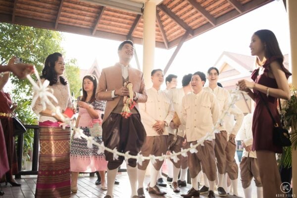 The bride's family hold a white garland chain across the path to stop the groom at the door games at Dusit Thani Hua Hin