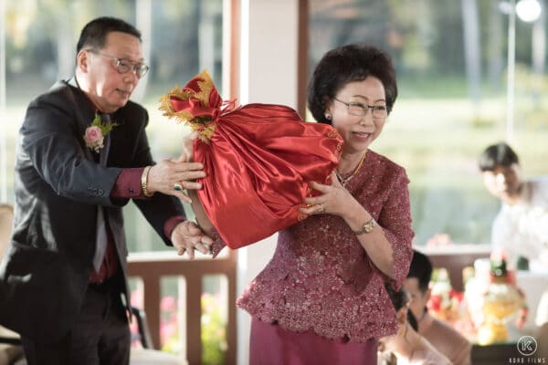 The bride's parents lift the Sin Sod dowry wrapped in red cloth, pretending it is heavy, at a Thai engagement ceremony at Dusit Thani Hua Hin