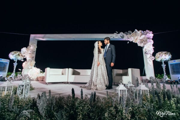 Bride and groom on a white floral stage at their evening Walima in Hua Hin