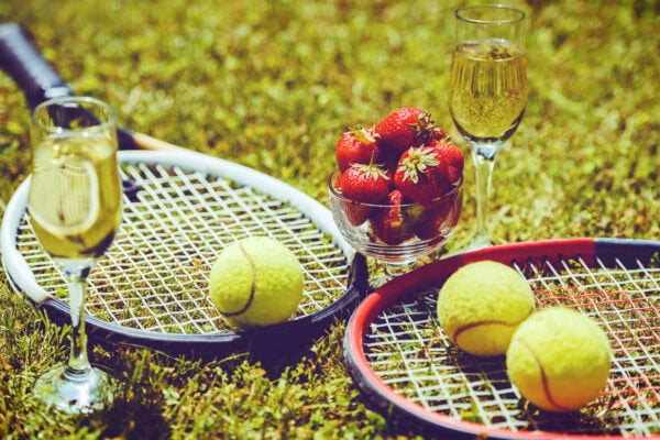 Tennis game. Strawberries, champagne and tennis balls with rackets on the green grass. Sport, recreation concept Tennis game. Strawberries, champagne and tennis balls with rackets on the green grass. Sport, recreation concept