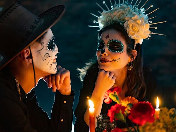 pexels-photo-7706435-7706435 Couple in Dia de los Muertos style makeup celebrating with candles and flowers.