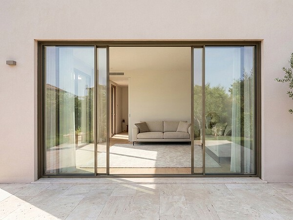 Aluminium sliding glass doors on a Dubai villa exterior, opening to a living room with terracotta pot and olive tree
