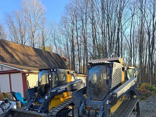 Two John Deere tracked loaders parked in the yard, one with a bucket and one with pallet forks