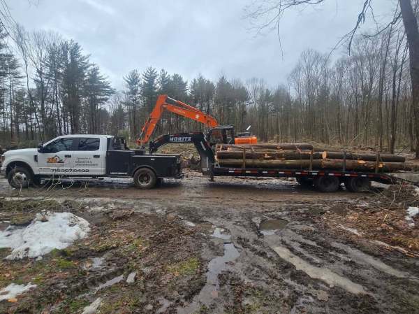 Excavation in Jamestown, NY T and L Services truck and gooseneck trailer being loaded by an orange Hitachi excavator on a muddy landing