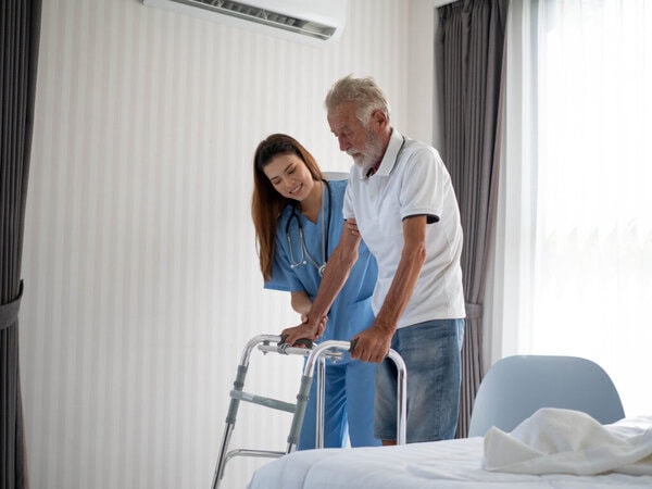 Pflegekraft unterstützt Senior bei der Körperpflege Pflegekraft hilft einem älteren Mann geradeaus zu gehen