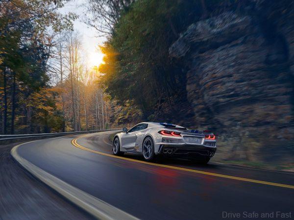 Rear 3/4 view of the 2024 Chevrolet Corvette E-Ray 3LZ convertible in Silver Flare with Electric Blue stripe package driving on curved mountain road. Pre-production model shown. Actual production model may vary. Model year 2024 Corvette E-Ray available 2023.